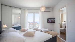 Quarto moderno com uma cama grande, luminária de cabeceira, televisão e vista da cidade pela janela.