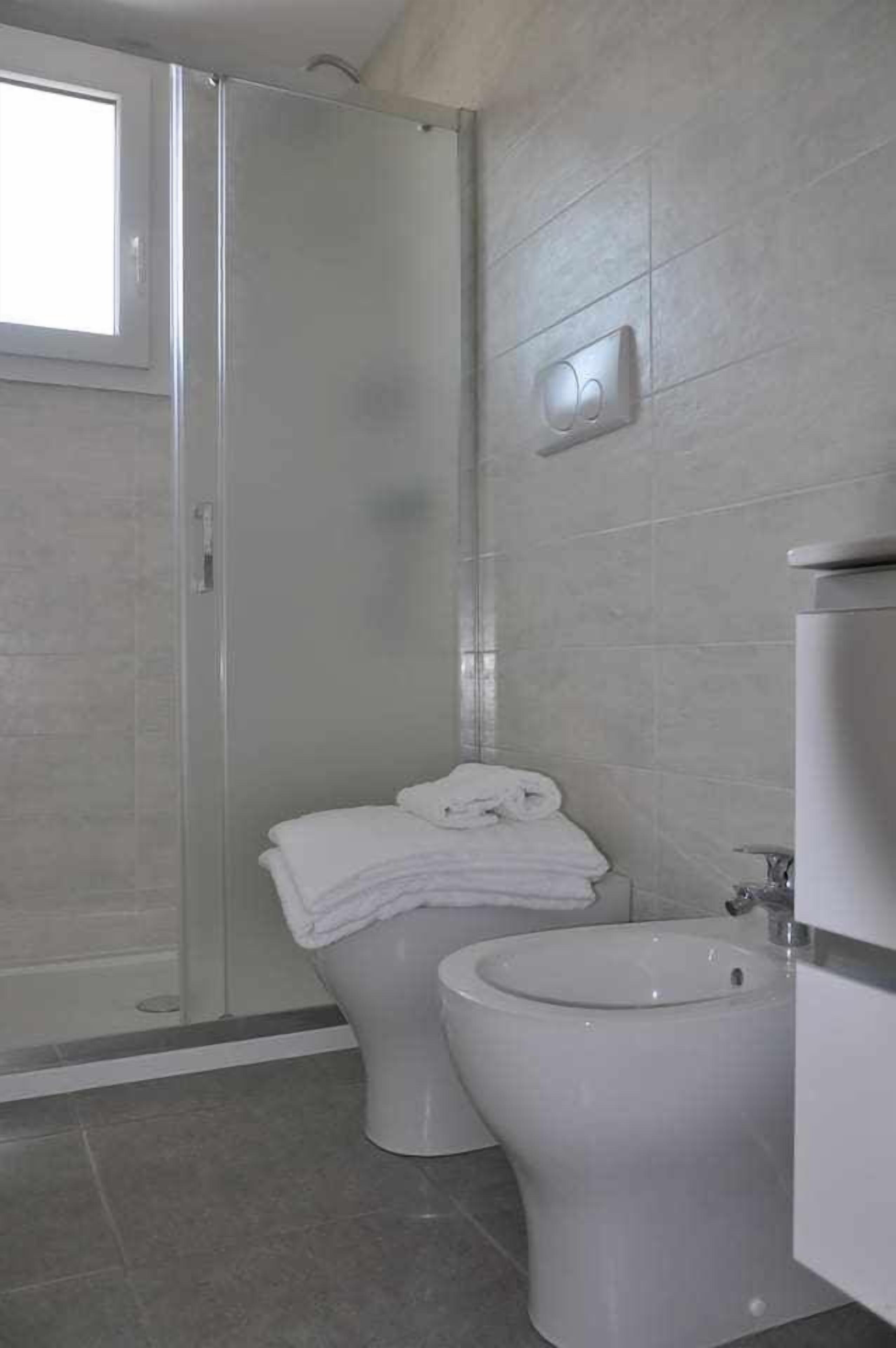 A bathroom with a shower, toilet, bidet, and a window.