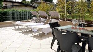 Un patio al aire libre con sillones de sol, una mesa de vidrio y sillas.