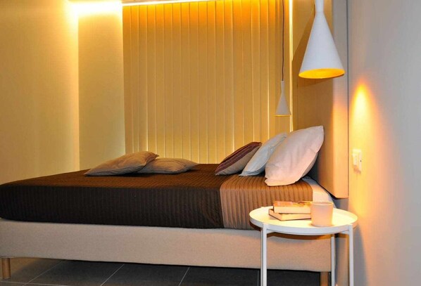 A modern bedroom with a bed, pillows, a bedside table with a book, and a pendant light.