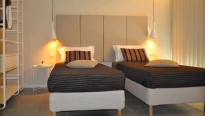 Habitación doble con dos camas, cada una con una almohada y una mesita de noche con lámpara.