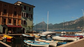 A marina with various boats docked, a building with multiple windows, and a mountainous backdrop. - Casa Bella: Charming Apartment with a Lake View (Bardolino)