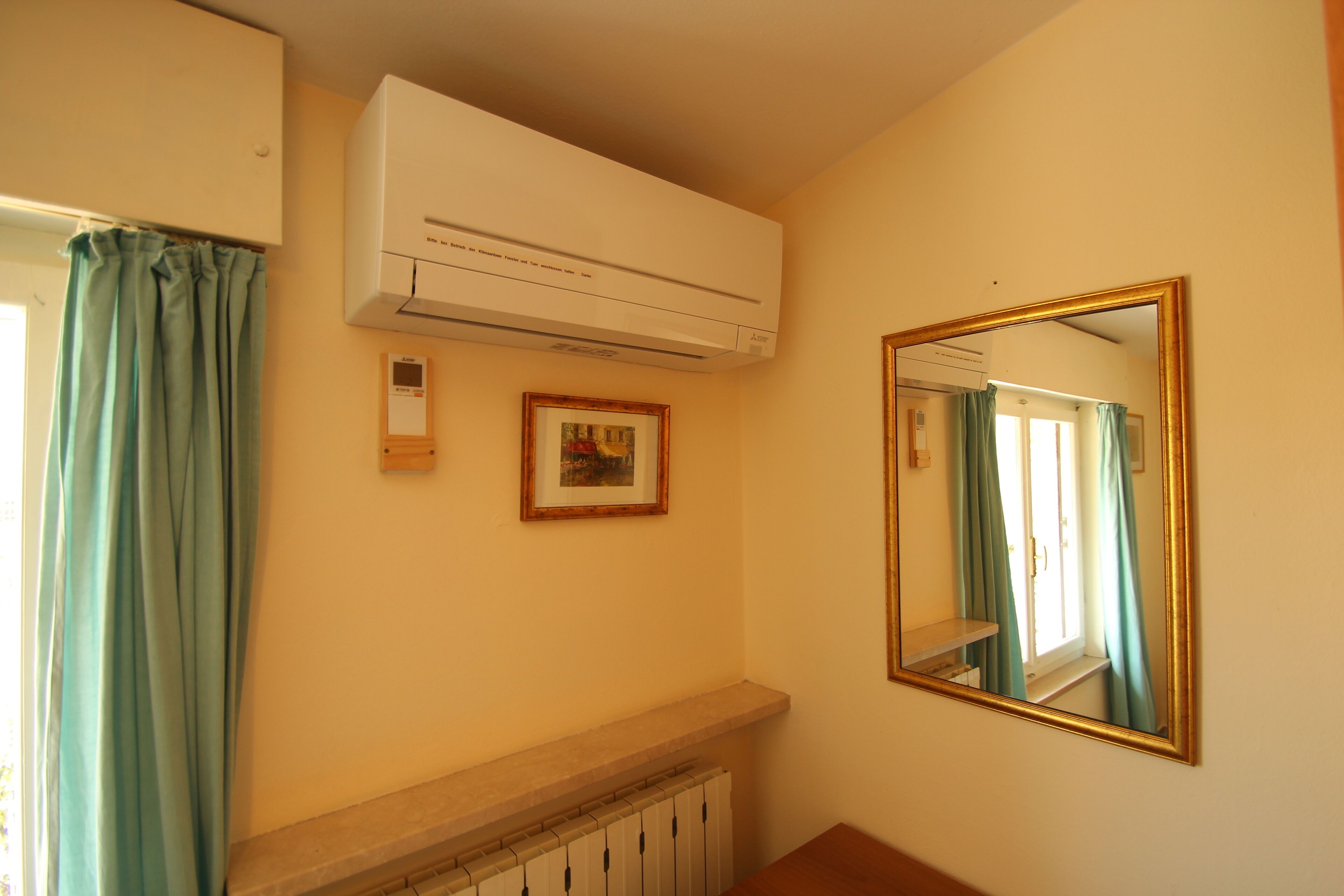 Un baño con aire acondicionado blanco, un cuadro enmarco, un espejo y una ventana con cortinas.