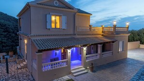 Une maison à deux étages dotée d’un balcon, d’un escalier en pierre et d’un éclairage extérieur.