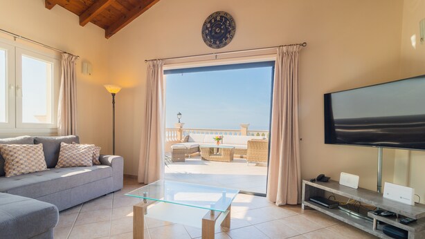 Un salon comprenant un canapé, une table basse en verre, un téléviseur à écran plat et un balcon aménagé avec du mobilier d’extérieur.