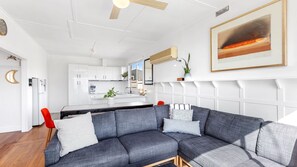 Ein modernes Wohnzimmer mit einem grauen Ecksofa, einem roten Sessel und einer Küche im Hintergrund.