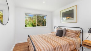 A bedroom with a bed, a window, a bedside table, a lamp, and a framed picture on the wall. - Ocean's 8 (Marengo)