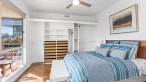 Een slaapkamer met een bed, een plafondventilator, een schilderij en uitzicht op de omgeving.