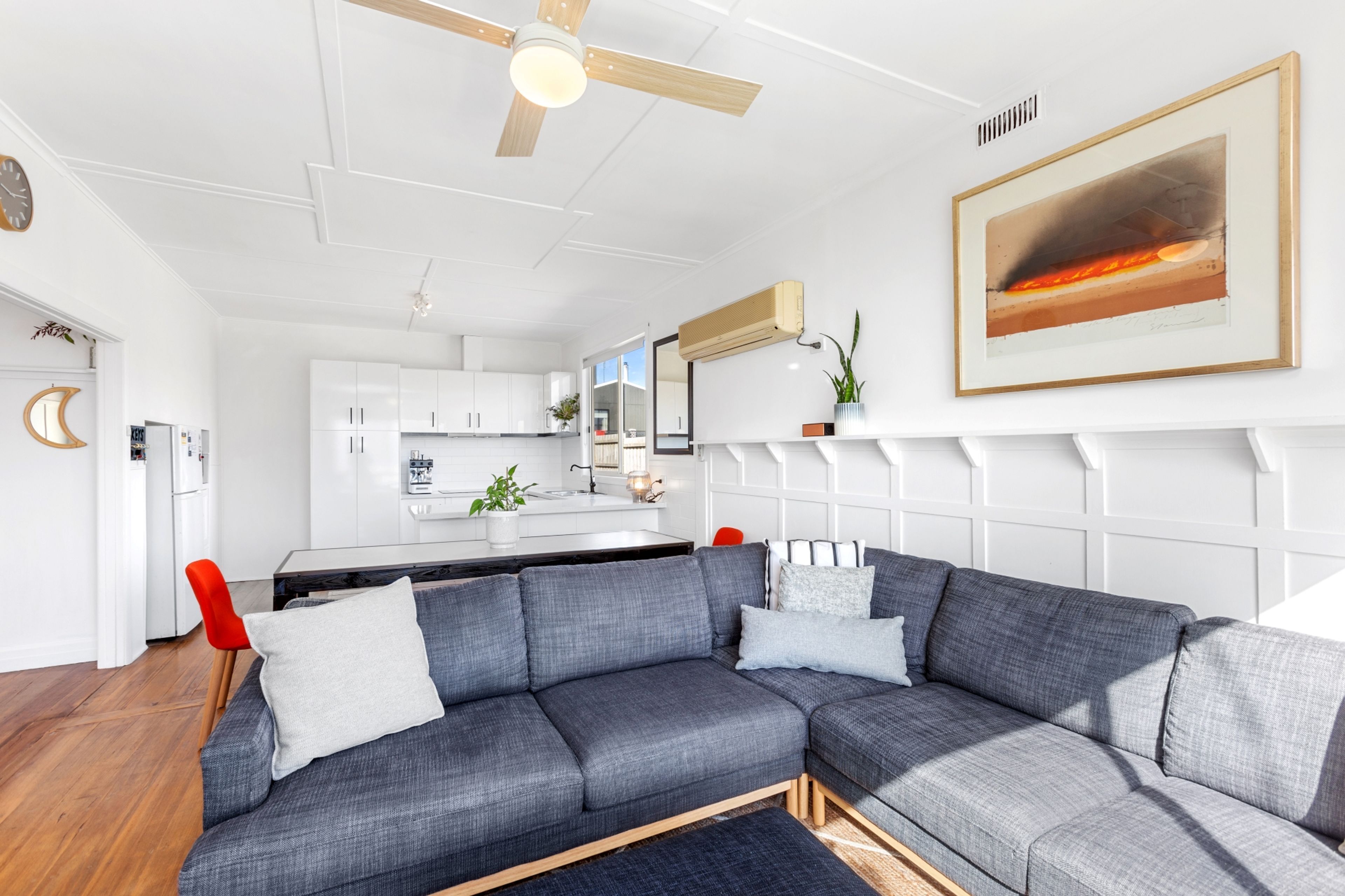A modern living room with a sectional sofa, a ceiling fan, and a kitchen in the background.
