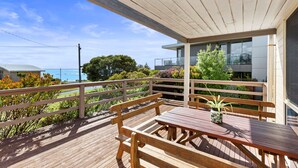 Una terraza de madera con una mesa y bancos, con vistas a un cuerpo de agua y follaje.