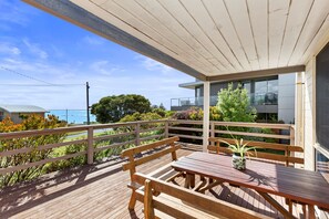 Una terraza de madera con una mesa y bancos, con vistas a un cuerpo de agua y follaje.
