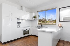 Una cocina moderna con armarios blancos, horno empotrado y ventana con vistas al exterior.