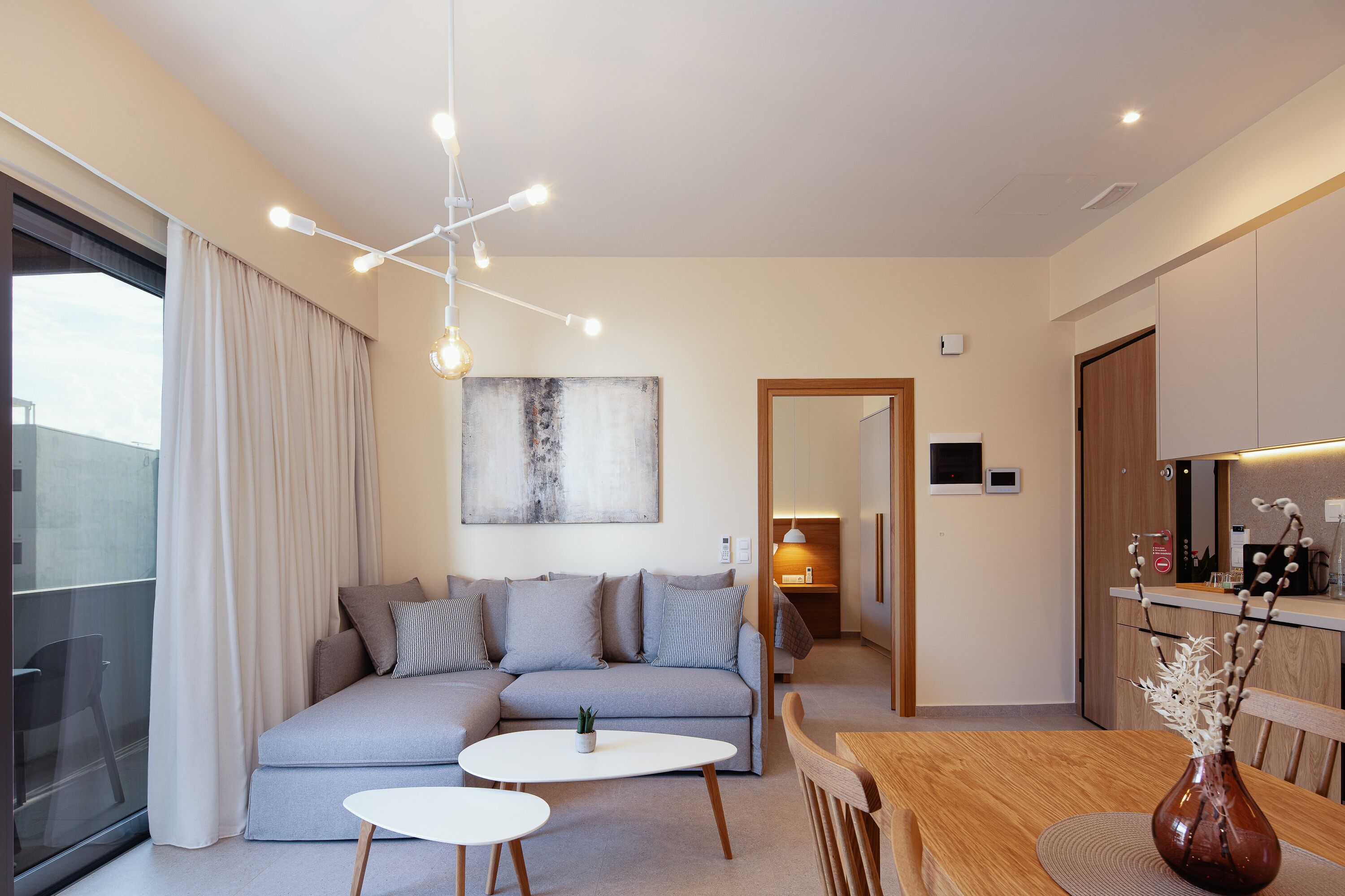 A modern living room with a sofa, two small tables, a wooden dining table, and a vase with branches.