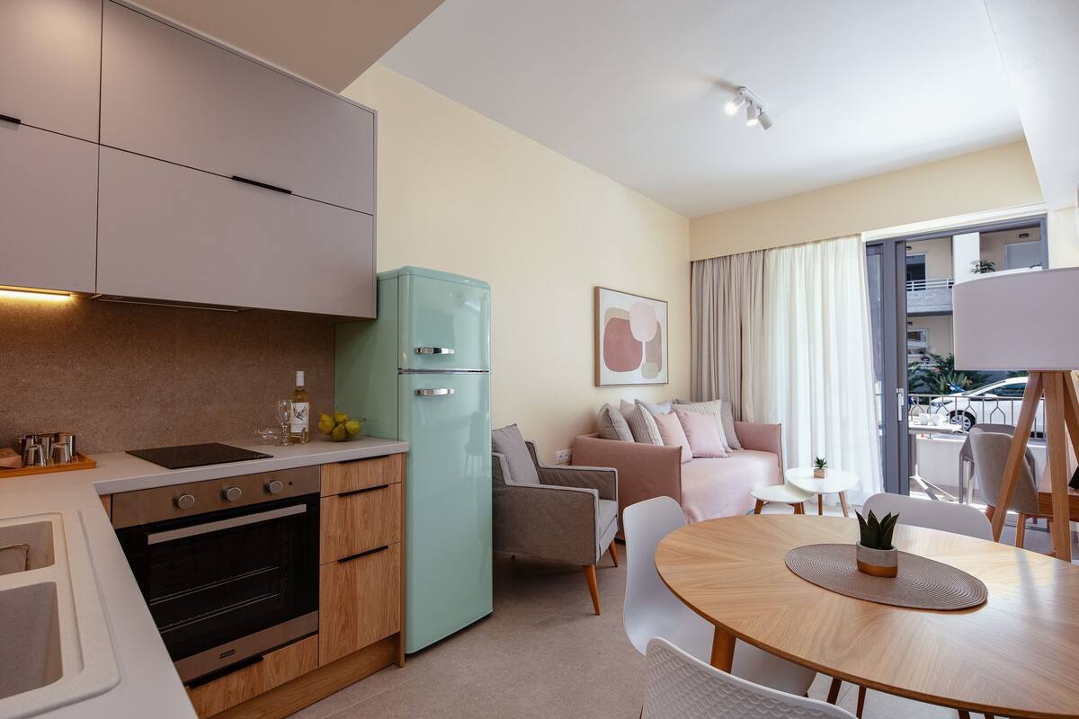 A modern kitchen with a built-in oven, a light green refrigerator, and a dining area with a round wooden table and white chairs.