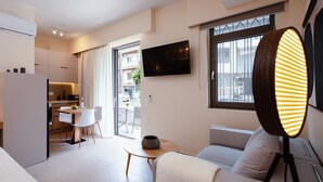 Una sala de estar moderna con un sofá, una mesa de comedor con sillas, un televisor montado en la pared y un gran ventanal con cortinas.