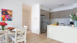 Una cocina moderna con una isla central, electrodomésticos de acero inoxidable y un comedor con mobiliario blanco.