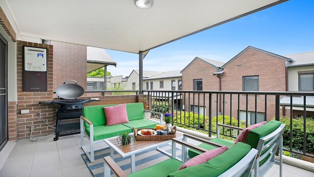Un balcón con asientos acolchados verdes, una parrilla y vistas a casas vecinas.