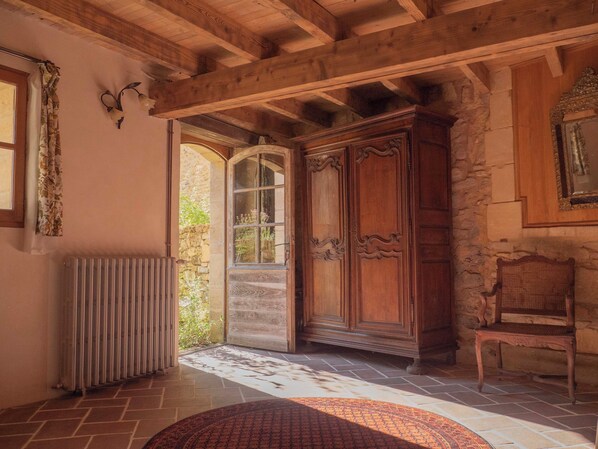 A rustic room with a wooden ceiling, a large wooden wardrobe, a wicker chair, and a radiator.