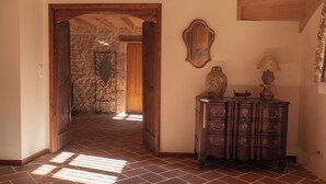 Une pièce avec une porte en bois donnant sur un mur de pierre, un meuble en bois avec des tiroirs et une lampe posée sur une table.
