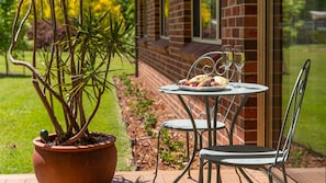 Eine Terrasse mit Tisch für zwei Personen, einem Blumentopf und einer Ziegelwand im Hintergrund.