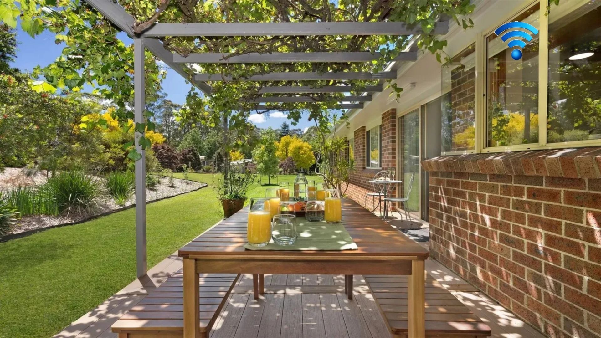 An outdoor patio with a wooden table set for breakfast, surrounded by a garden and a brick wall.