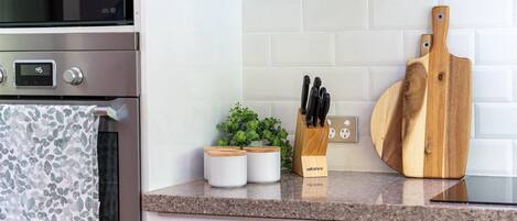 Een keuken met een roestvrijstalen oven, een digitale klok, een houten snijplank, een messenblok en een kleine potplant.