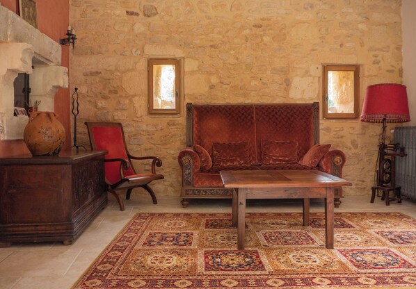 A room with a stone wall, a wooden table, a red sofa, a red chair, and a patterned rug. - "La Chapelle aux Roses" (Le Bugue)