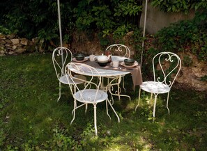 A white metal outdoor table and chairs set on a grassy lawn with a stone wall and foliage in the background. - "La Chapelle aux Roses" (Le Bugue)