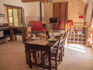 A rustic dining area with a wooden table set for four, a stone wall, and a television in the background.