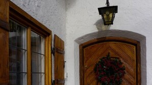 Una porta de fusta amb una corona de llorer, una finestra amb persianes i un fanal penjat a la paret.
