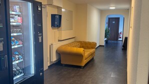 A hallway with a vending machine, a yellow sofa, a fire extinguisher, and a door labeled "28". - Capitol Zentrum - 24h - (Friedrichshafen)