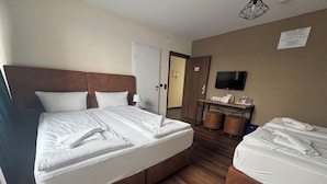A hotel room with a large bed, a smaller bed, a desk with a flat-screen TV, and a door leading to another room. - Capitol Zentrum - 24h - (Friedrichshafen)