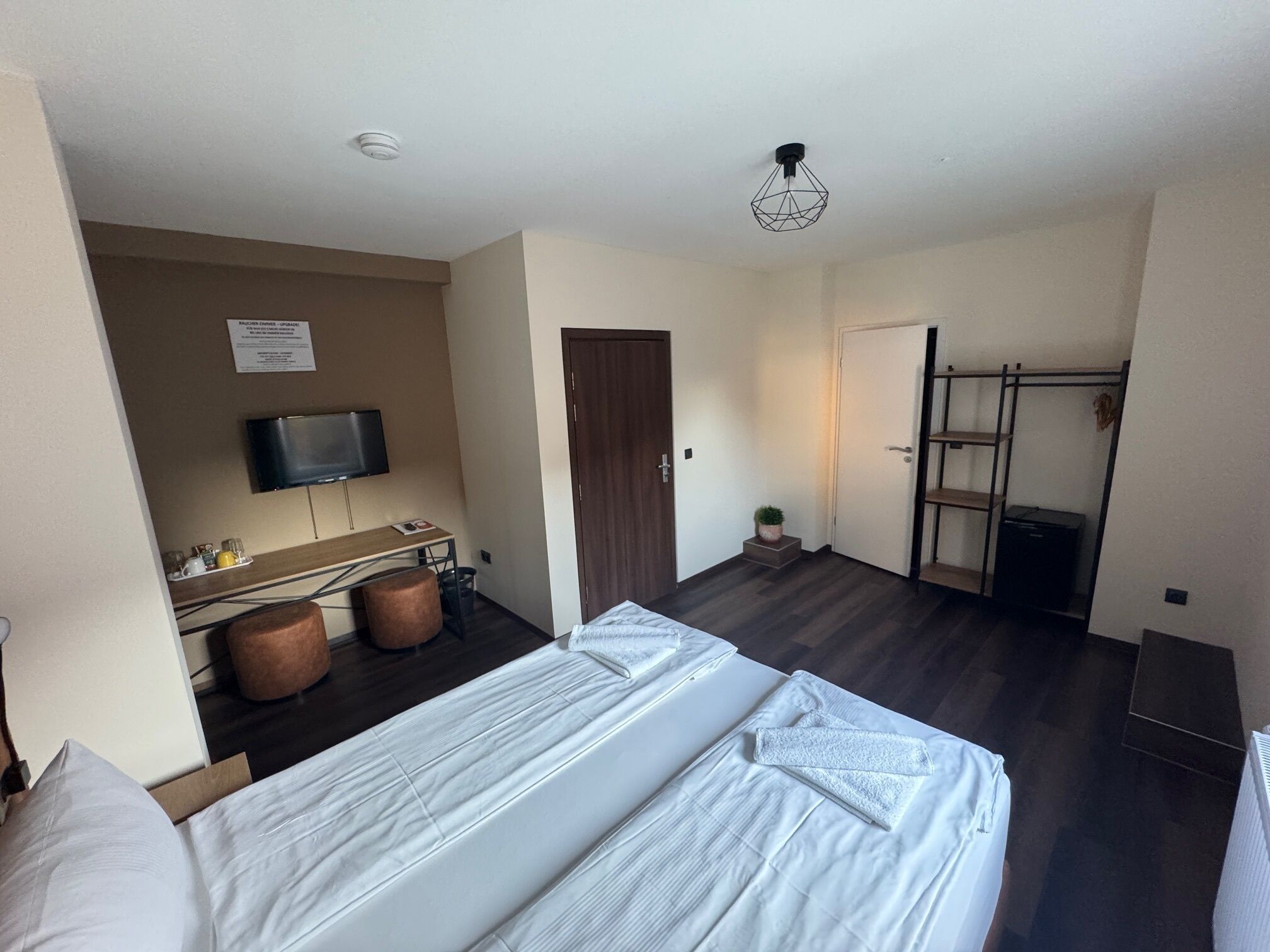 Ein Hotelzimmer mit Bett, Schreibtisch, Flachbildfernseher, einer kleinen Pflanze und einer Tür zu einem Balkon.
