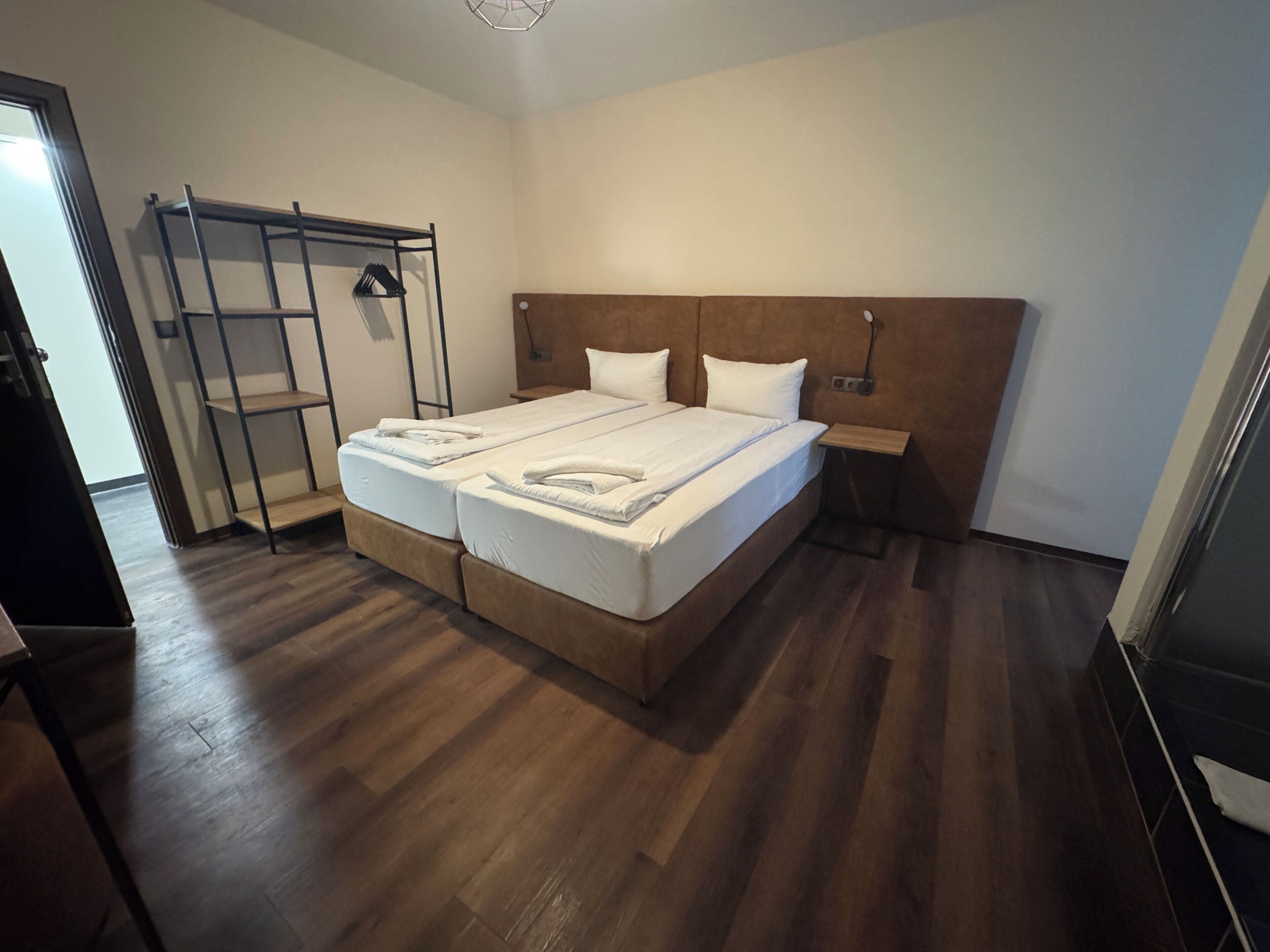 A double bed with white linens, a wooden headboard, and a bedside table with a lamp.