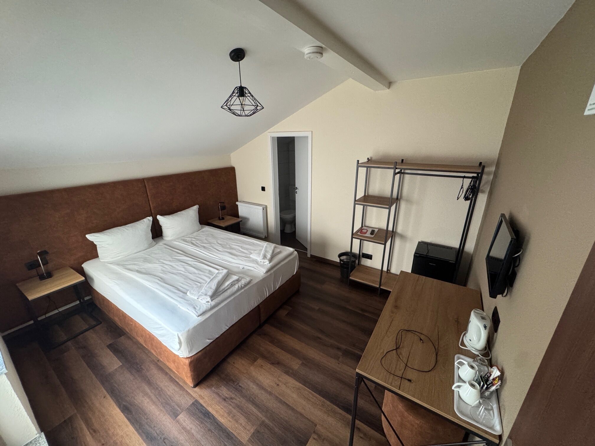 Ein Hotelzimmer mit einem großen Bett, einem Holztisch, einer Regalwand und einer Deckenleuchte.