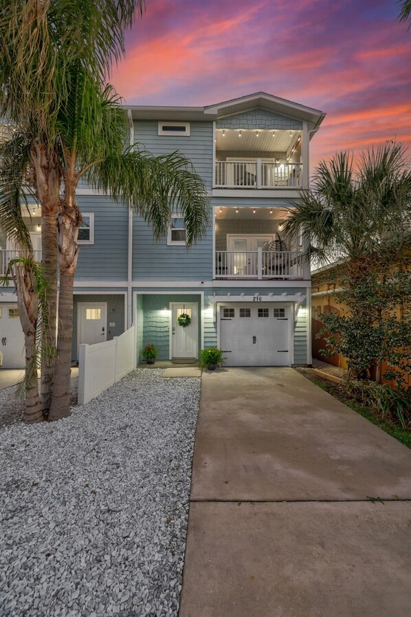 A two-story residential building with a garage, a balcony on the upper floor, and a driveway leading to the entrance.