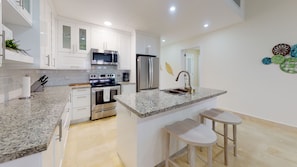 A modern kitchen with white cabinets, stainless steel appliances, a granite countertop, and a small bar area with stools.