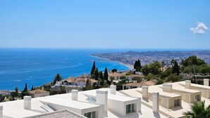 A coastal residential area with modern white buildings, a clear blue sky, and a view of the sea and distant cityscape. - Stunning sea views @ Stupa hills (Benalmádena)