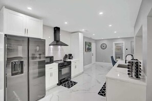 A modern kitchen with white cabinetry, stainless steel appliances, and a black range hood.