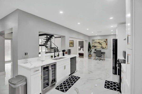 A modern kitchen with white cabinetry, a built-in dishwasher, and a stainless steel range hood.