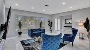 A modern living room with a blue sofa, a round coffee table, and a blue armchair. - LUX 6BR 4Bath Htd Pool & SPA Mini Golf G-Room (Deerfield Beach)