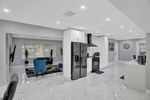 A modern kitchen with white cabinets, a stainless steel refrigerator, and a black range hood. - LUX 6BR 4Bath Htd Pool & SPA Mini Golf G-Room (Deerfield Beach)