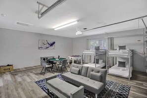 Una sala moderna con un sofá, una mesa de centro y una mesa de comedor con sillas. Hay una litera con escalera y una ventana con persianas.