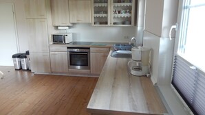 A modern kitchen with wooden cabinets, a microwave, a stove, and a coffee maker. - Ferienwohnung in zentraler, ländlicher Lage (Groven)