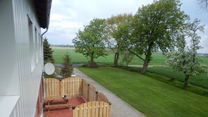 A patio with a wooden fence, a red rug, and a satellite dish on the building. - Ferienwohnung in zentraler, ländlicher Lage (Groven)