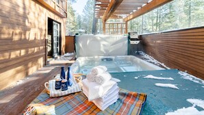 Un espace avec un bain à remous, doté de murs en bois, d’un coin salon abrité et offrant une vue sur les arbres.