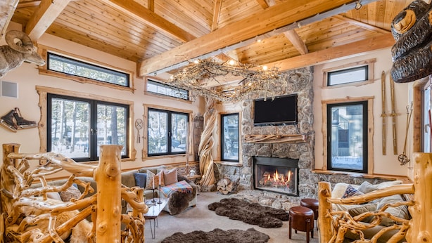 Un intérieur rustique avec une cheminée en pierre, des poutres en bois et un coin salon confortable agrémenté d’un tapis en fourrure.