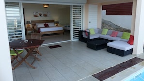 A hotel room with a bed, a sofa, a table, and a pool area. - Villa Alizés 8 pers. 4 air-conditioned bedrooms (Le Gosier)