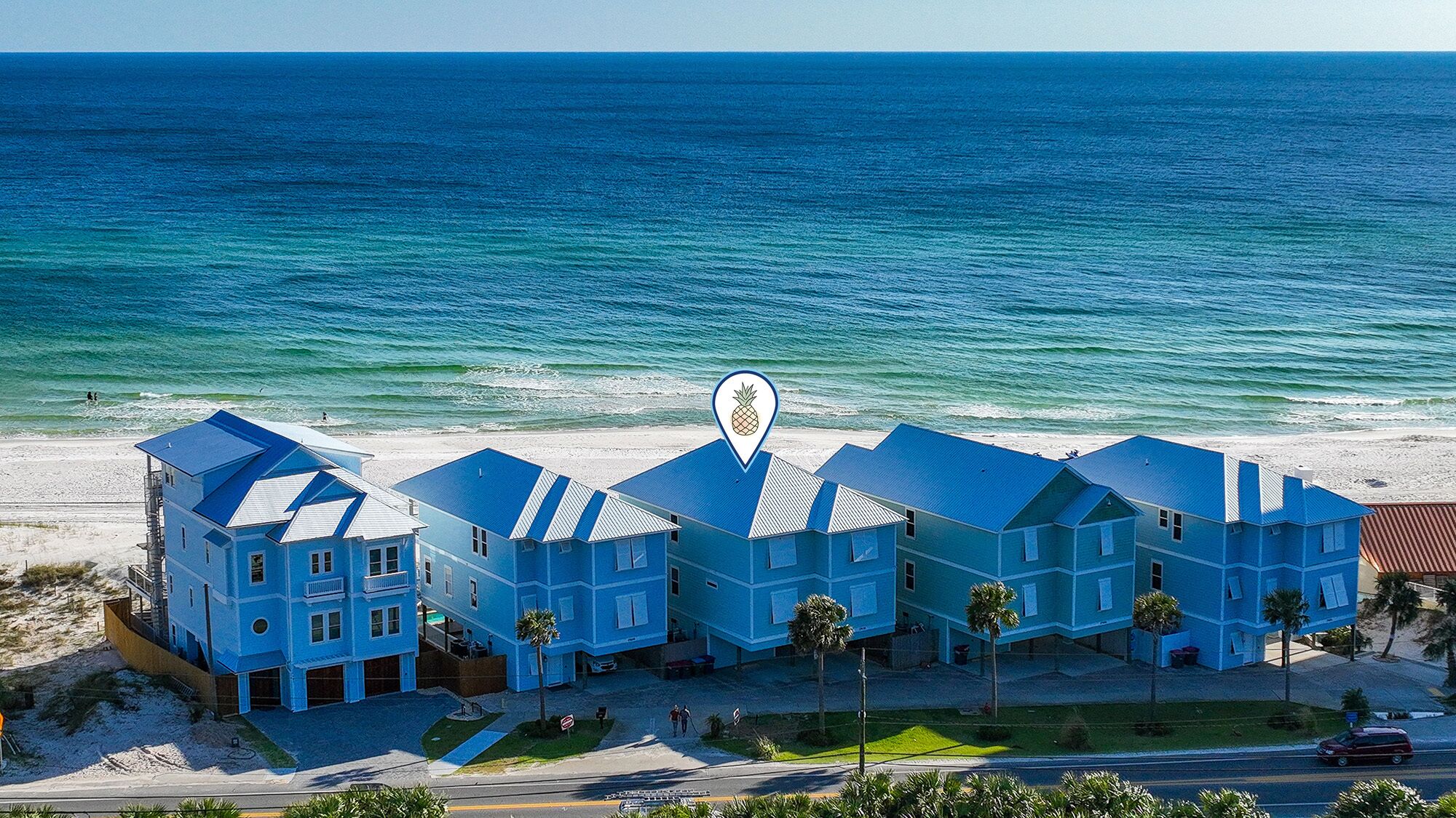 Et hotel ved stranden med flere blå bygninger, en sandstrand og havet i baggrunden.