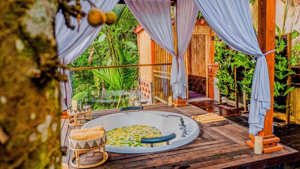 Una terraza de madera con un jacuzzi rodeado de plantas de bambú y una valla de madera.